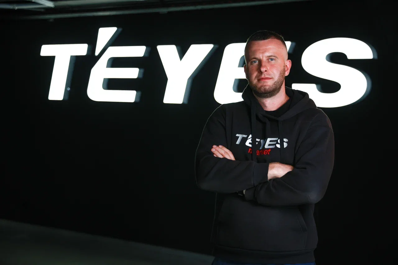 Сотрудник в фирменной одежде TEYES Market на фоне логотипа